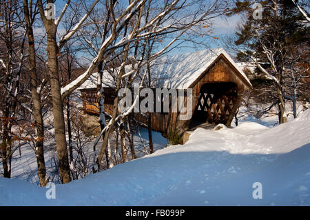 Des empreintes de pas menant au pont couvert de neige en bois traverse le fleuve gelé sur une journée ensoleillée après les chutes de neige dans la région de Henniker, New Hampshire. Banque D'Images