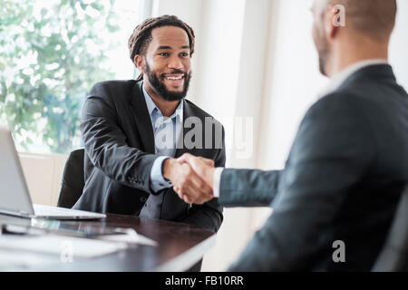 Smiling businessmen shaking hands in office Banque D'Images