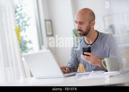 Man with laptop and holding smart phone at table Banque D'Images