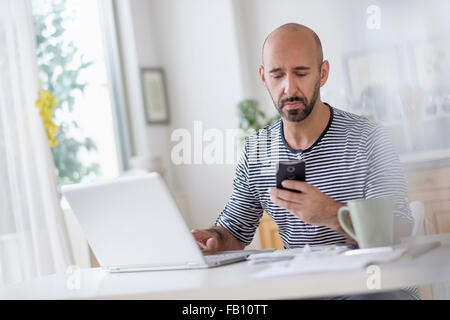 Man with laptop and holding smart phone at table Banque D'Images