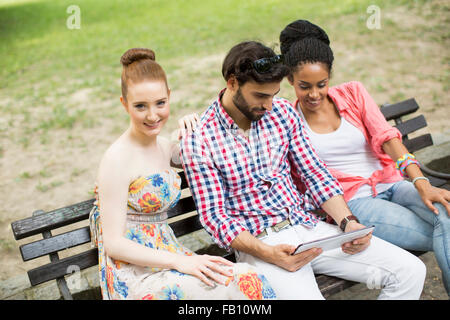 Amis multiraciale, assis sur le banc avec tablet Banque D'Images