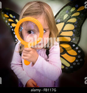 Girl (2-3) wearing les ailes de papillon à la loupe à travers Banque D'Images