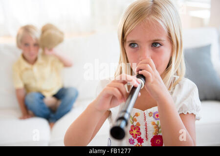 Girl (6-7) playing flute and boy (4-5) sitting on sofa Banque D'Images