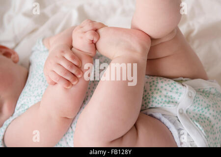 Baby Girl (12-17 mois) couché avec mains sur pieds Banque D'Images