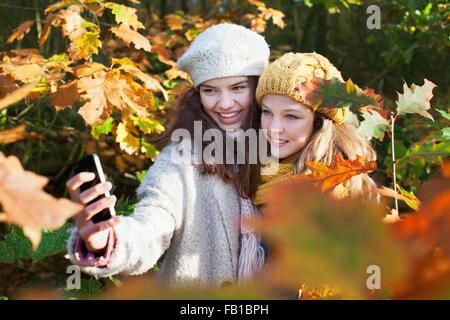 High angle view of teenage girls parmi les feuilles d'automne en utilisant smartphone pour prendre smiling selfies