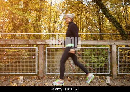 Senior female nordic walker marcher sur la passerelle du parc Banque D'Images