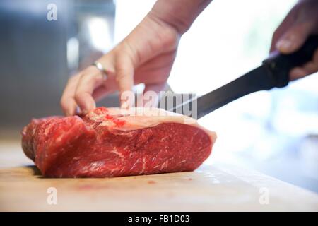 Close up of butchers mains slicing raw steak sur bloc de boucher Banque D'Images