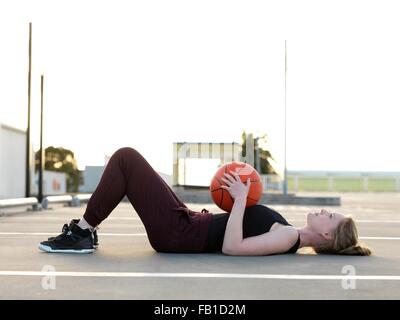 Jeune joueur de basket-ball féminin allongée sur le dos en faisant une pause Banque D'Images