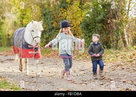 Garçon et sœur conduisant le long de poney country lane Banque D'Images