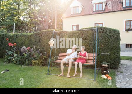 Couple, la détente sur swing siège dans jardin Banque D'Images