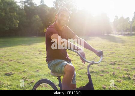 Portrait of young man on bicycle in sunlit park Banque D'Images