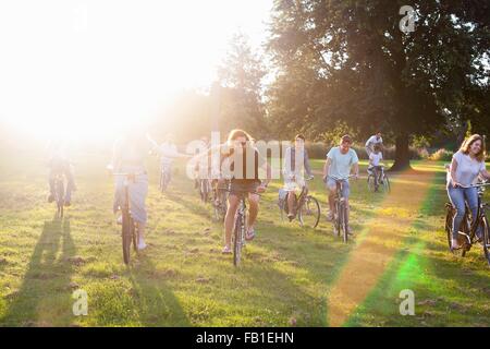 La foule d'amis adultes arrivant à bicyclette dans le parc Sunset Party Banque D'Images