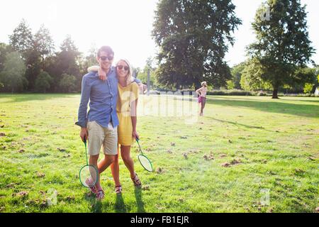 Jeune couple romantique avec raquettes de badminton in sunlit park Banque D'Images