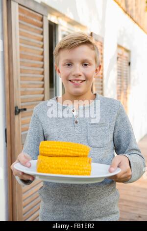 Portrait of boy carrying plate d'épis de maïs pour barbecue dans jardin Banque D'Images