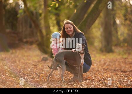 Mid adult woman and baby daughter petting dog in autumn park Banque D'Images