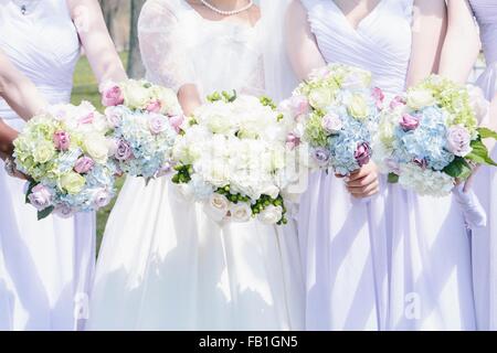 Portrait de la jeune mariée et demoiselles côte à côte holding bouquets de fleurs Banque D'Images