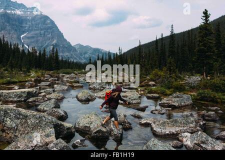 Side view of mid adult woman walking on rocky rivière, lac Moraine, Banff National Park, Alberta Canada Banque D'Images