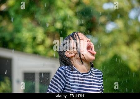 Jeune fille au jardin, attraper l'eau qui tombe dans la bouche Banque D'Images