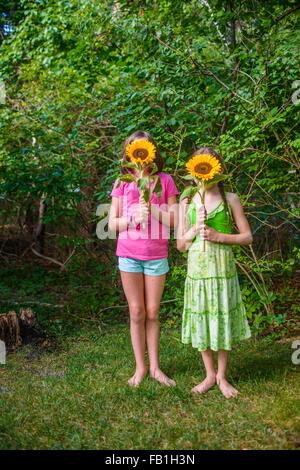 Deux jeunes filles holding sunflowers en face de visages Banque D'Images