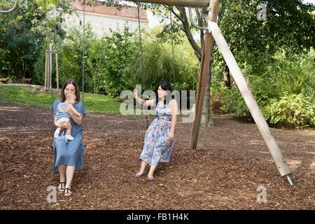 Jeune femme avec mère et fille de bébé assis sur des balançoires dans le parc Banque D'Images