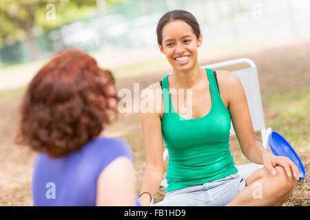 Jeune femme assise jambes croisées de parler à un ami, smiling Banque D'Images