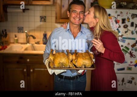 Portrait of mature couple holding roast chickens in kitchen Banque D'Images