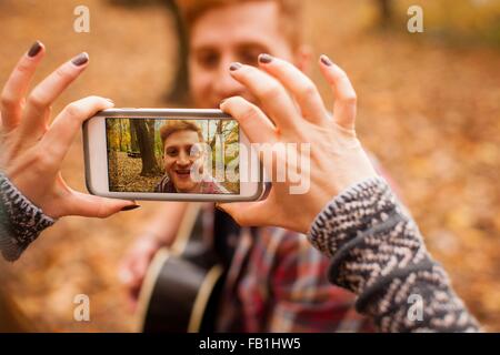 Mains de young woman photographing boyfriend sur smartphone en forêt d'automne Banque D'Images