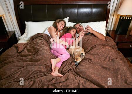 Portrait de jeune fille dans le lit des parents et le chien looking at smartphone smiling Banque D'Images