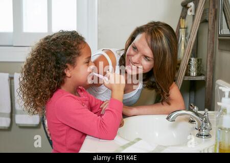 Mère et fille dans la salle de bains lavabo à se brosser les dents face à face smiling Banque D'Images