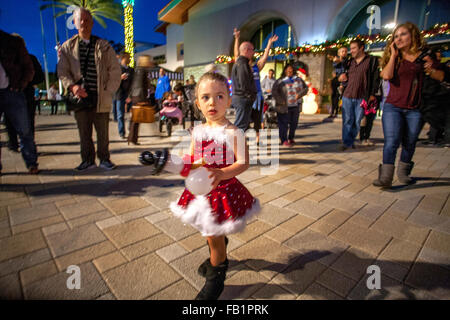 Habillé dans son costume de Noël et de transporter un ballon, une fillette de 3 ans a l'air en admiration à son environnement à une piscine de nuit festival à Laguna Niguel, CA. Banque D'Images