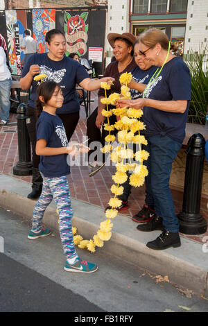 Une famille hispanique marigold jaune cordes fleurs en papier à Jour des Morts (Dia de muertos) cérémonies à Santa Ana, CA. Le souci est un symbole traditionnel de respect pour les morts et la maison de l'accent sur les rassemblements de la famille et des amis de prier pour un Banque D'Images