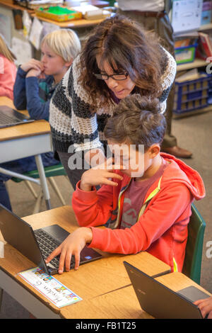 Un enseignant de troisième année d'une aide aux étudiants hispaniques entrez les informations dans leurs ordinateurs portables Chromebook de Google dans un San Clemente, CA, école primaire de classe. Remarque la concentration. Banque D'Images