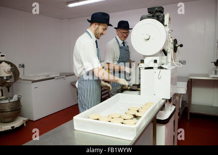 2 les hommes travailler et prendre des tartes de porc dans une usine. Banque D'Images