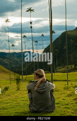 Fille avec veste gris assis sur l'herbe verte regarder de hauts palmiers dans la vallée de Cocora Banque D'Images