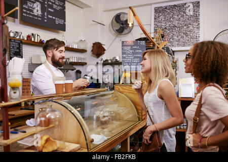 Tourné d'une des jeunes femmes les amis de passer une commande dans un café. Café Waiter taking order de deux jeunes femmes les costumers stan Banque D'Images