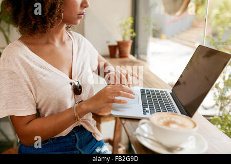 Portrait of young woman working on laptop while sitting in cafe. African girl en utilisant un ordinateur portable avec une tasse de café sur Banque D'Images