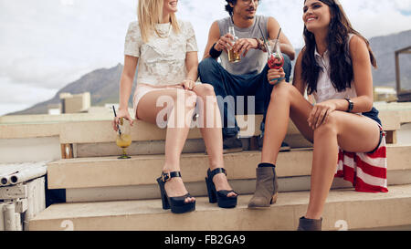 Cropped shot of young friends sitting on steps and having cocktails pendant une partie. Les jeunes ayant une partie sur le toit. Banque D'Images