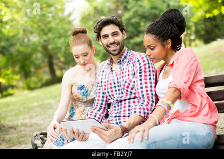 Amis multiraciale, assis sur le banc avec tablet Banque D'Images