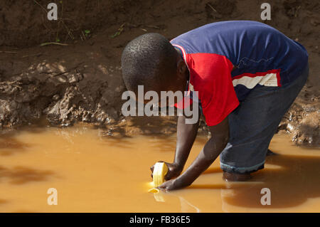 Jeune enfant obtenir de l'eau d'une rivière boueuse, au Kenya. Banque D'Images