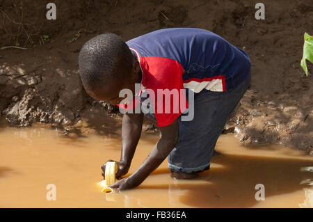 Jeune enfant obtenir de l'eau d'une rivière boueuse, au Kenya. Banque D'Images