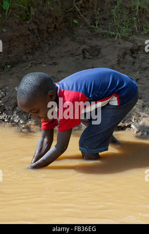 Jeune enfant obtenir de l'eau d'une rivière boueuse, au Kenya. Banque D'Images