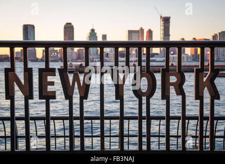 "New York" insérés dans les balustrades métalliques au World Financial Center Plaza au coucher du soleil avec la rivière Hudson et de Jersey City skyline Banque D'Images