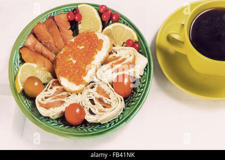 Sur la table sur un plat de céramique est le poisson, caviar, roule avec le poisson, les tomates, le citron. Next est une tasse de café noir. Banque D'Images