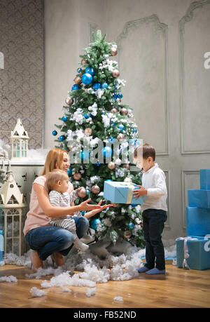 Jeune mère donnant un présent pour le fils aîné, baby boy touching bauble on Christmas Tree Banque D'Images