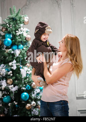 Jeune femme jouant avec petit-fils habillés en costume de singe à côté arbre de Noël Banque D'Images