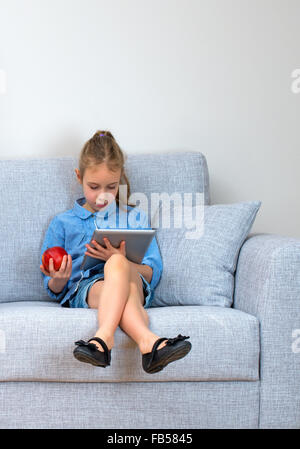 Petite fille assise sur le canapé et à l'aide de tablet pc. Banque D'Images