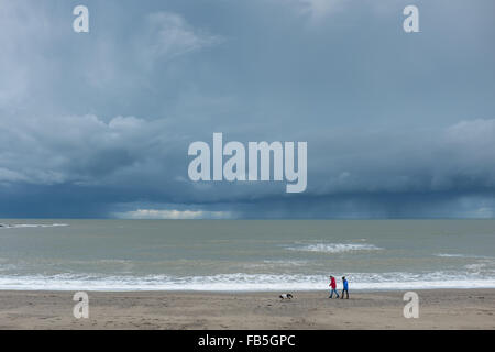 Aberystwyth, Pays de Galles, Royaume-Uni. 10 janvier 2016. Un couple marcher leur chien sur la plage à Aberystwyth aussi foncé rainclouds planent sur la mer. Credit : Alan Hale/Alamy Live News Banque D'Images