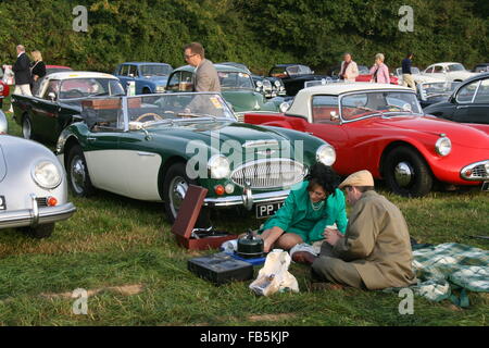 Un homme ET UNE FEMME DANS LA MODE VINTAGE UN PIQUE-NIQUE À GOODWOOD REVIVAL ENTOURÉ DE VOITURES CLASSIQUES Banque D'Images