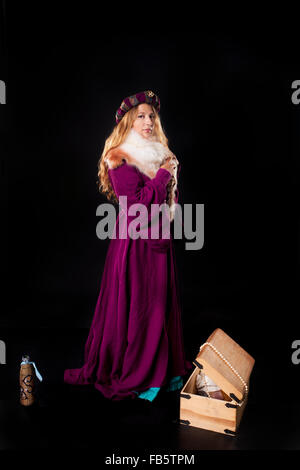 Portrait de studio de belle fille vêtue comme une noble dame médiévale en manteau de pourpre et la fourrure avec un coffre au trésor sur noir backg Banque D'Images