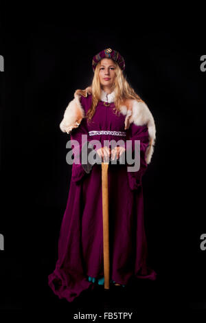 Studio photo de belle fille vêtue comme une noble dame médiévale dans un manteau s'appuyant sur les grands ax (fond noir) Banque D'Images